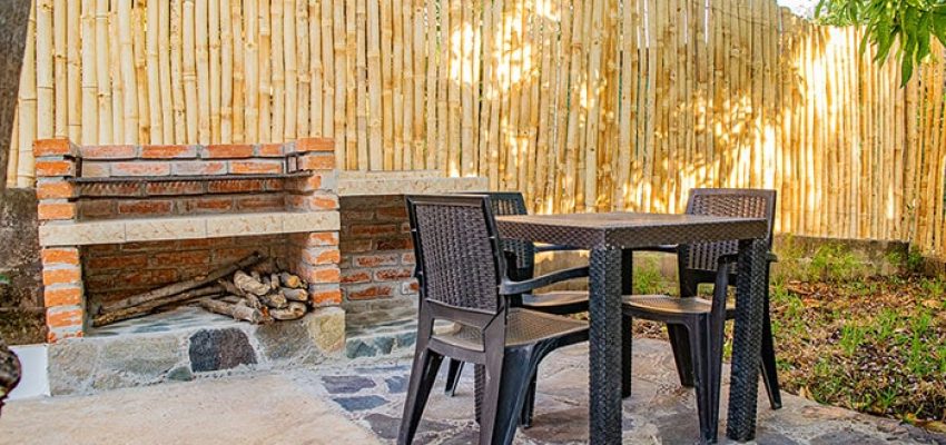 Muebles de exterior en zona de jardín con chimenea de madera y madera, ambiente rural y relajante, ideal para disfrutar del verano.