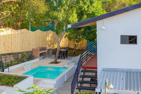 Piscina privada en jardín con zona de descanso y barbacoa para vacaciones en la playa.