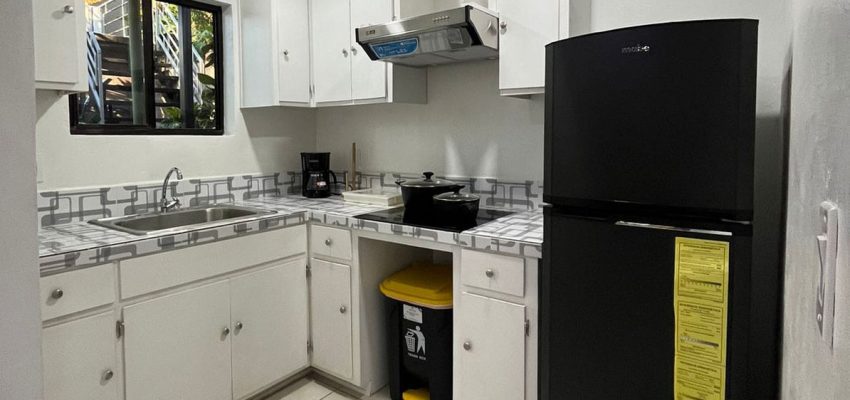 Cocina blanca moderna con horno y nevera negra, espacio bien iluminado y limpio.