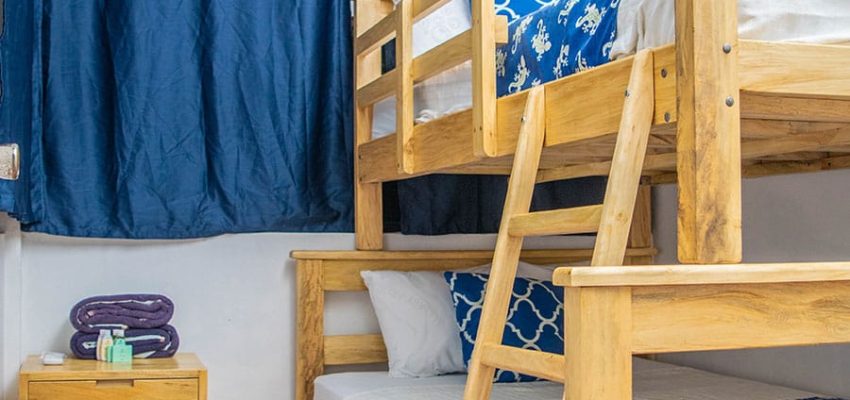 Cama doble con literas de madera en habitación de hotel con cortinas azules y aire acondicionado.