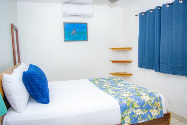 Cama con sábanas blancas y cojín azul en habitación con decoración con temática marina.