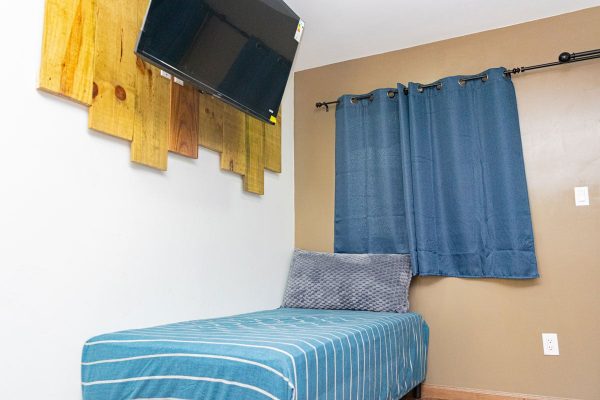 Zona de descanso con cama individual y cortinas azules, decoración moderna en habitación de surf en olas permanentes.