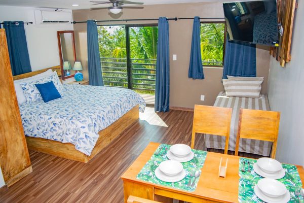 Conjunto de habitación con cama doble, ventanas con vistas a la naturaleza y decoración en tonos azules.