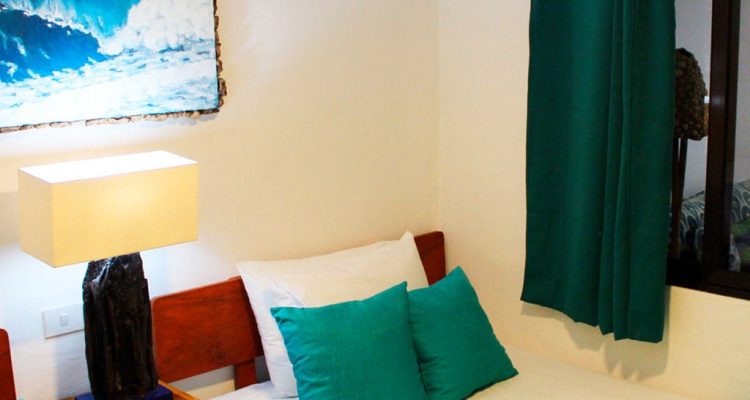 Cama doble con almohadas turquesas en habitación con decoración moderna y vista a la ventana.