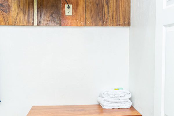 Televisión en pared con madera, muebles de madera, toallas blancas dobladas, decoración rústica en habitación, alojamiento de surf, Olas Permanentes.